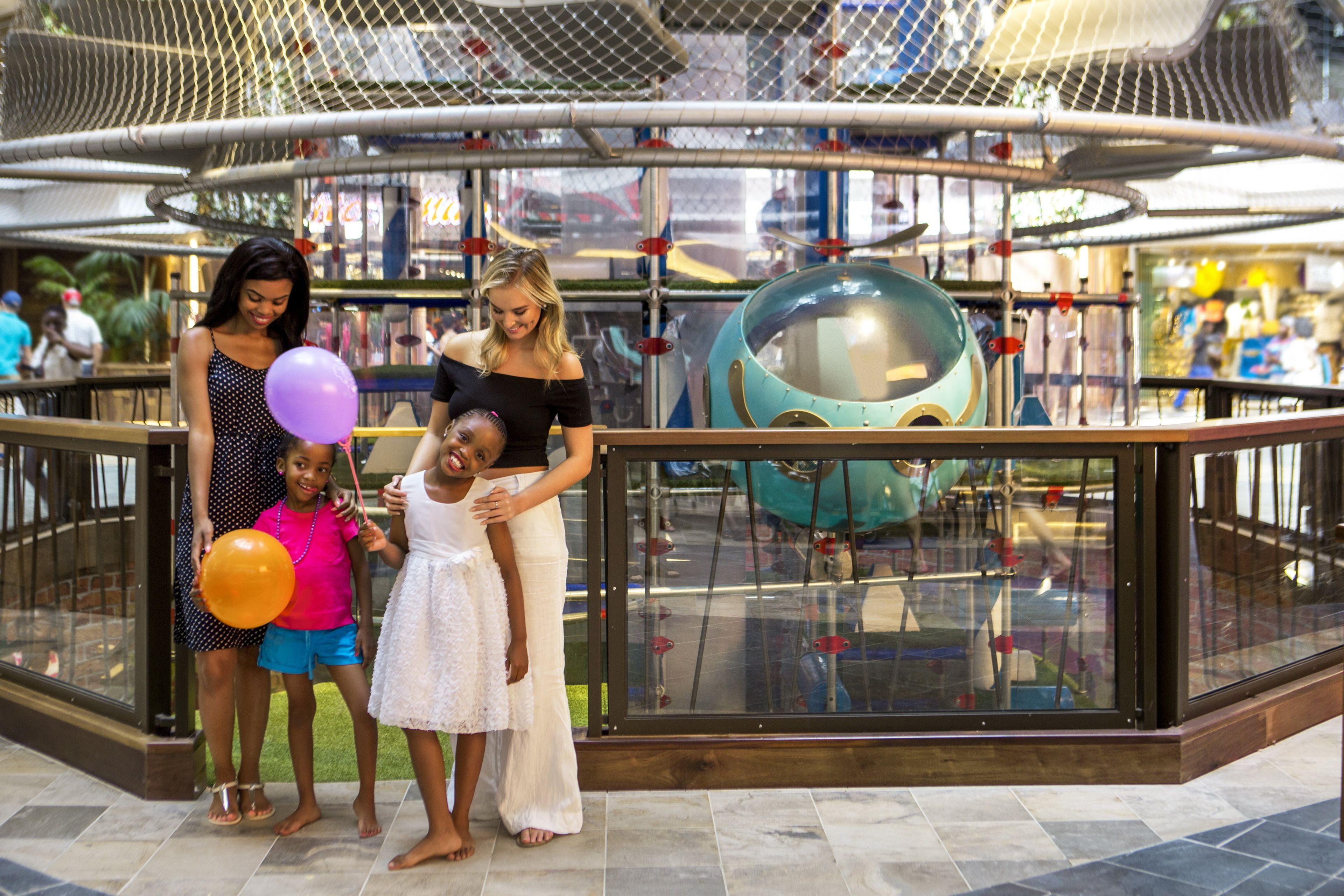 A shopping mall with a glass railing, a playground with a large ball, and people.