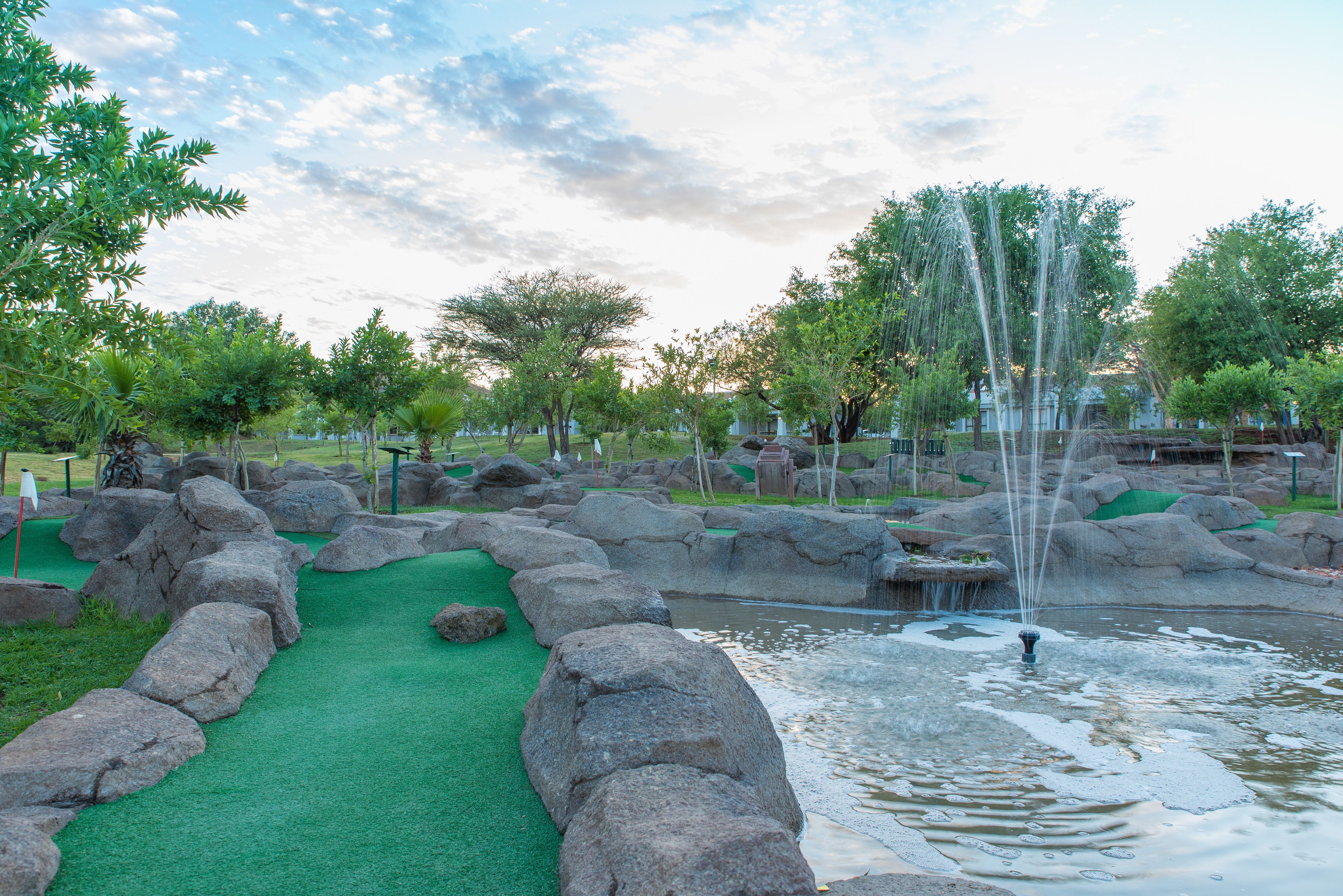 A miniature golf course with a putting green, water hazards, and a fountain.