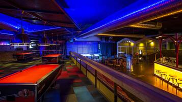 Un espace dédié à un billard, avec un tapis de jeu rouge, un bar avec des tabourets et un coin salon avec des tables et des chaises.