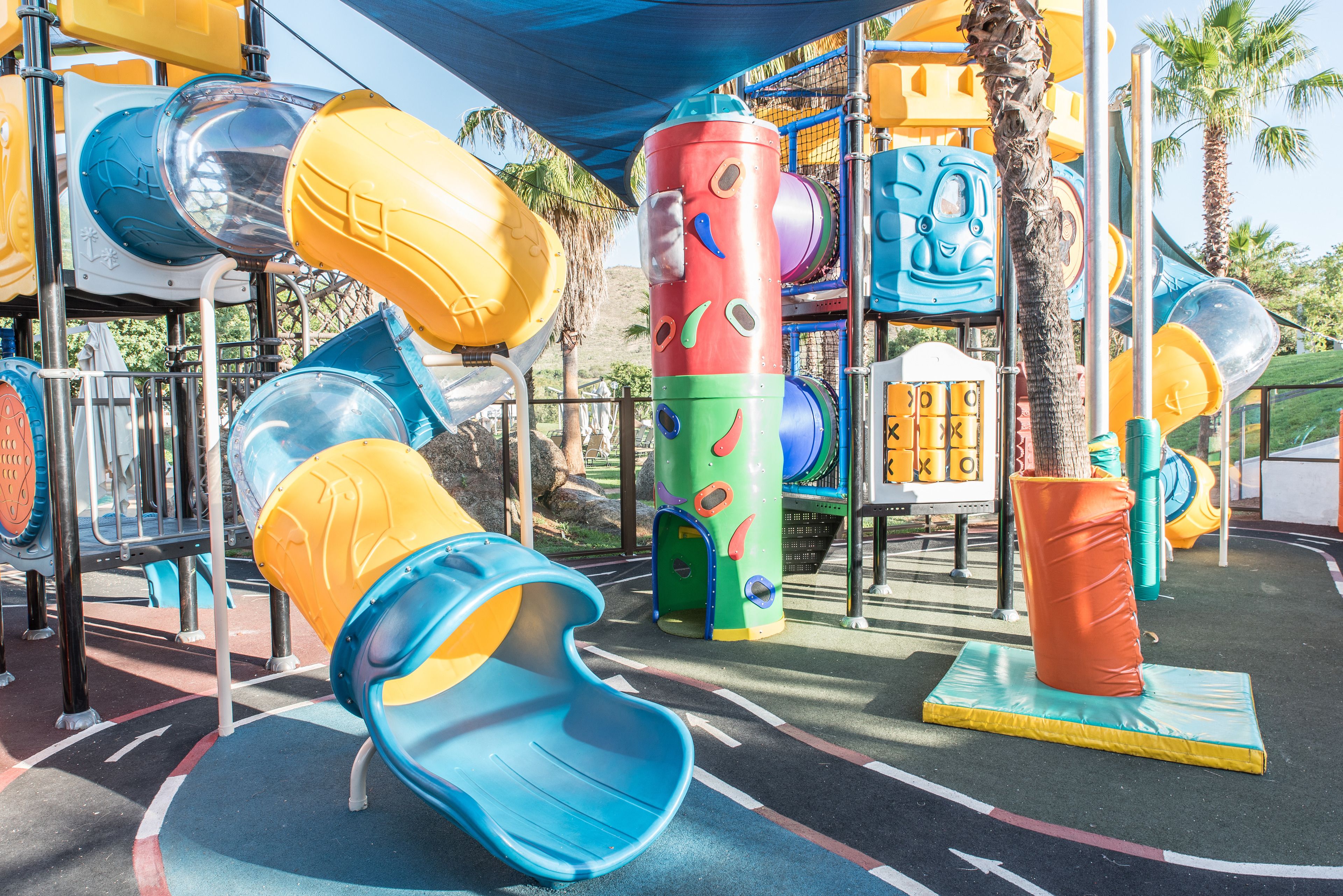 A playground with slides, climbing structures, and a palm tree.