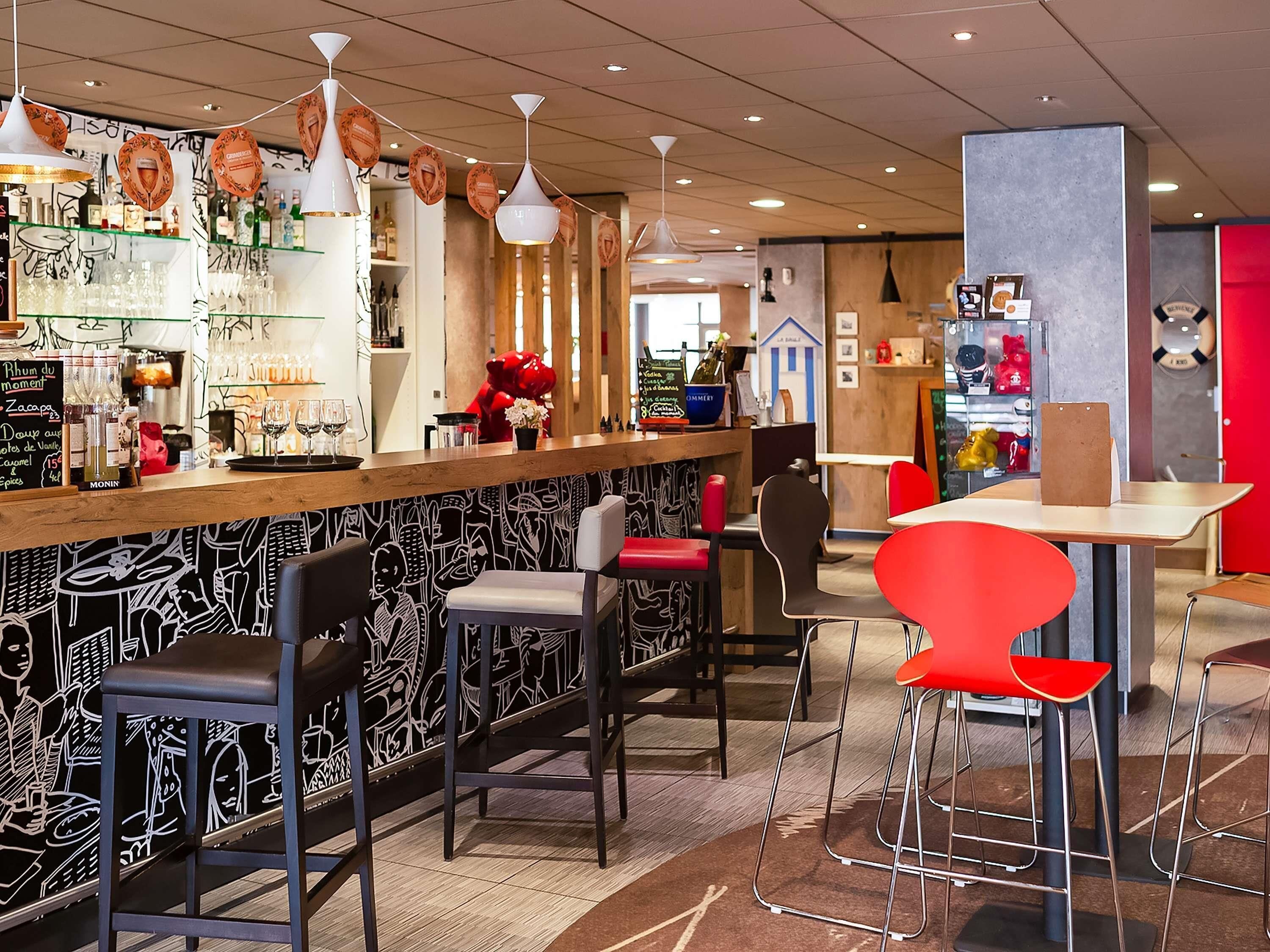 A bar area with stools, a counter with bottles, and a wall with a black and white pattern.