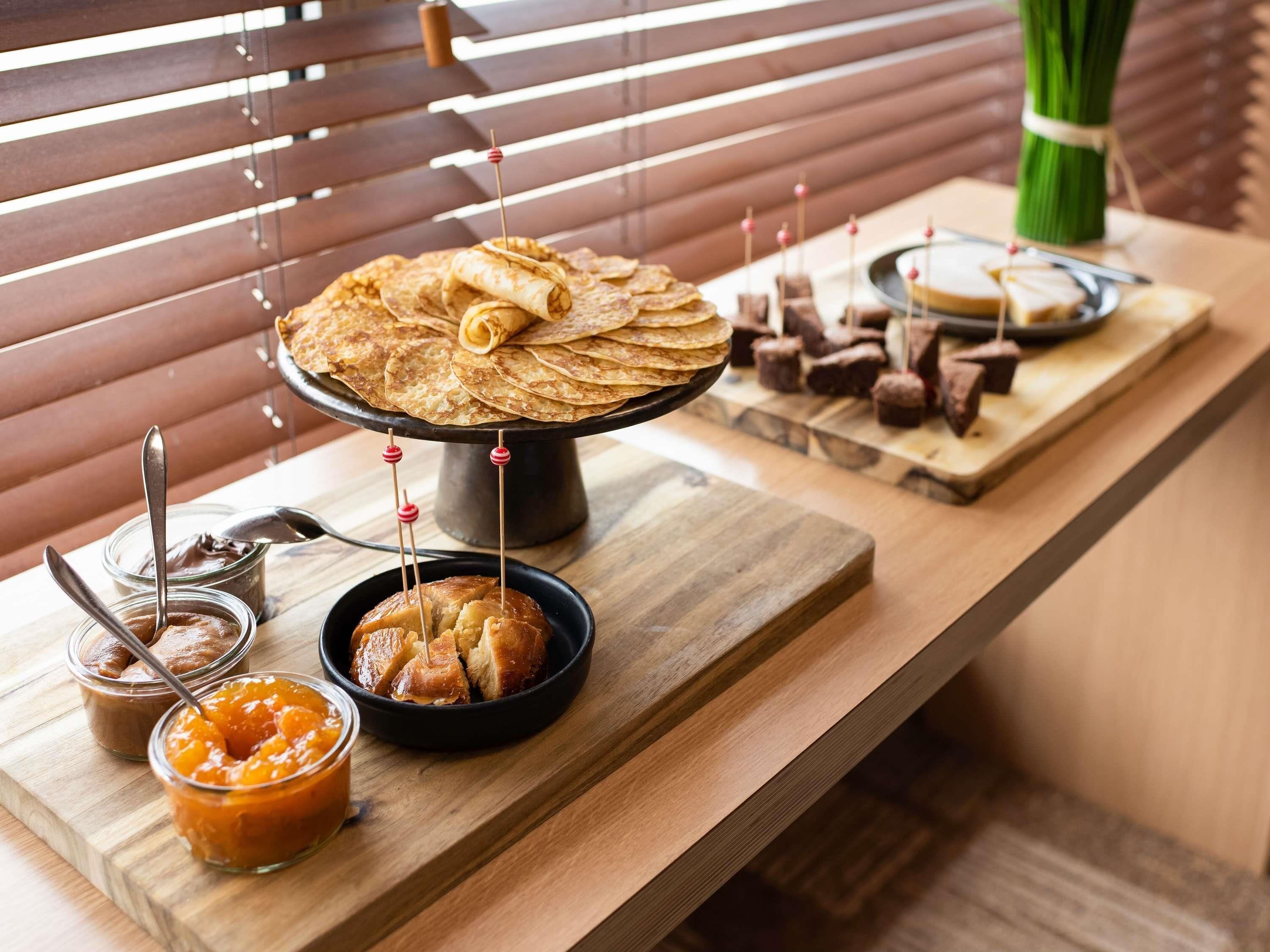 A wooden table with a variety of food items, including a large plate of flatbreads, a bowl of fruit, and several small containers of spreads.