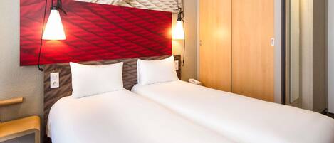 A hotel room with a large bed, two bedside lamps, a wooden wardrobe, and a red textured wall.