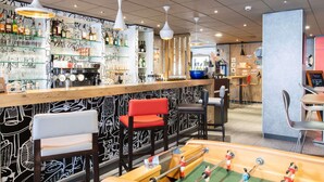 A bar area with a foosball table, bar stools, and shelves of bottles and glasses.