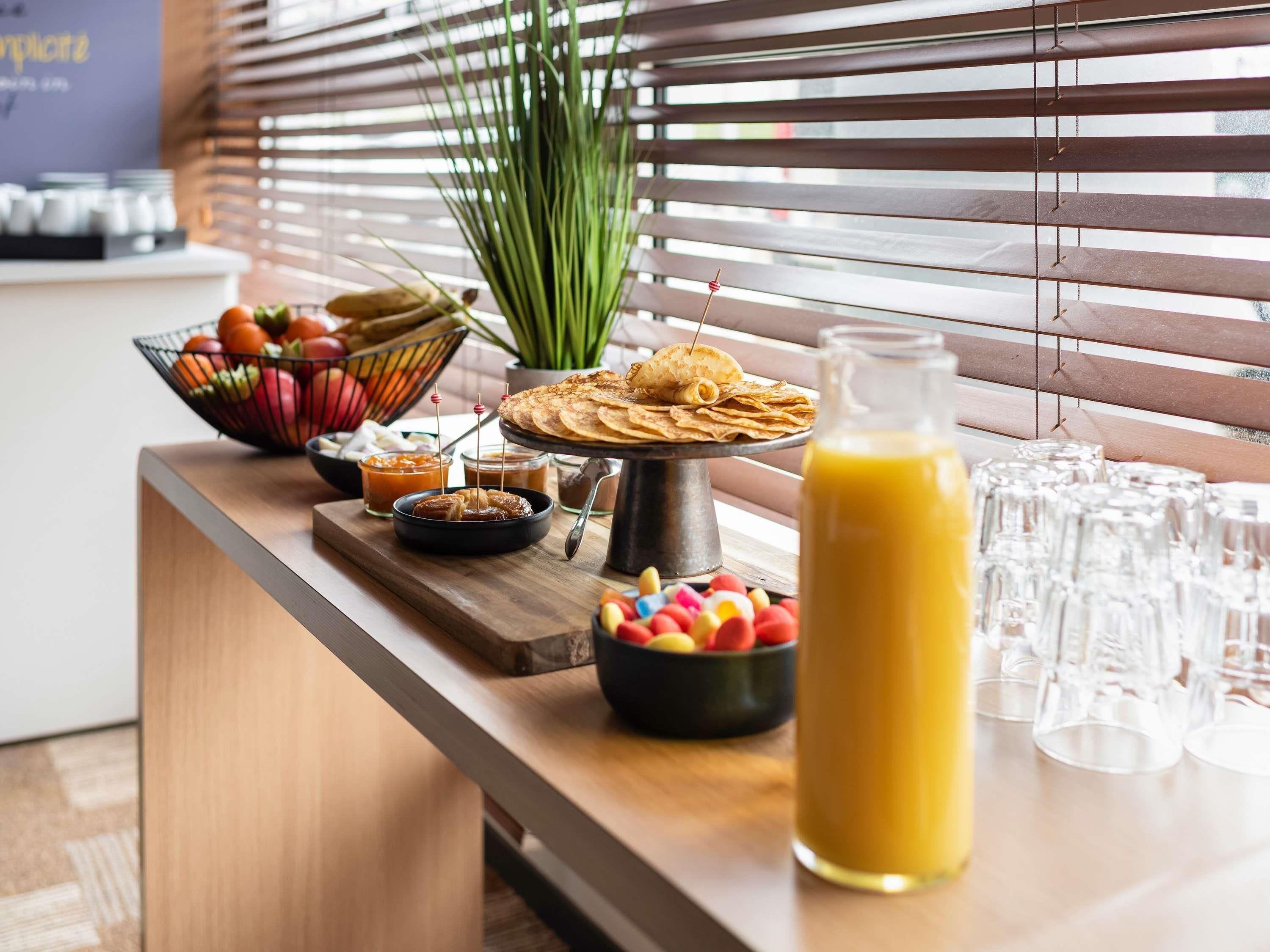 A breakfast buffet with various food items, a bottle of orange juice, and empty glasses on a wooden table.