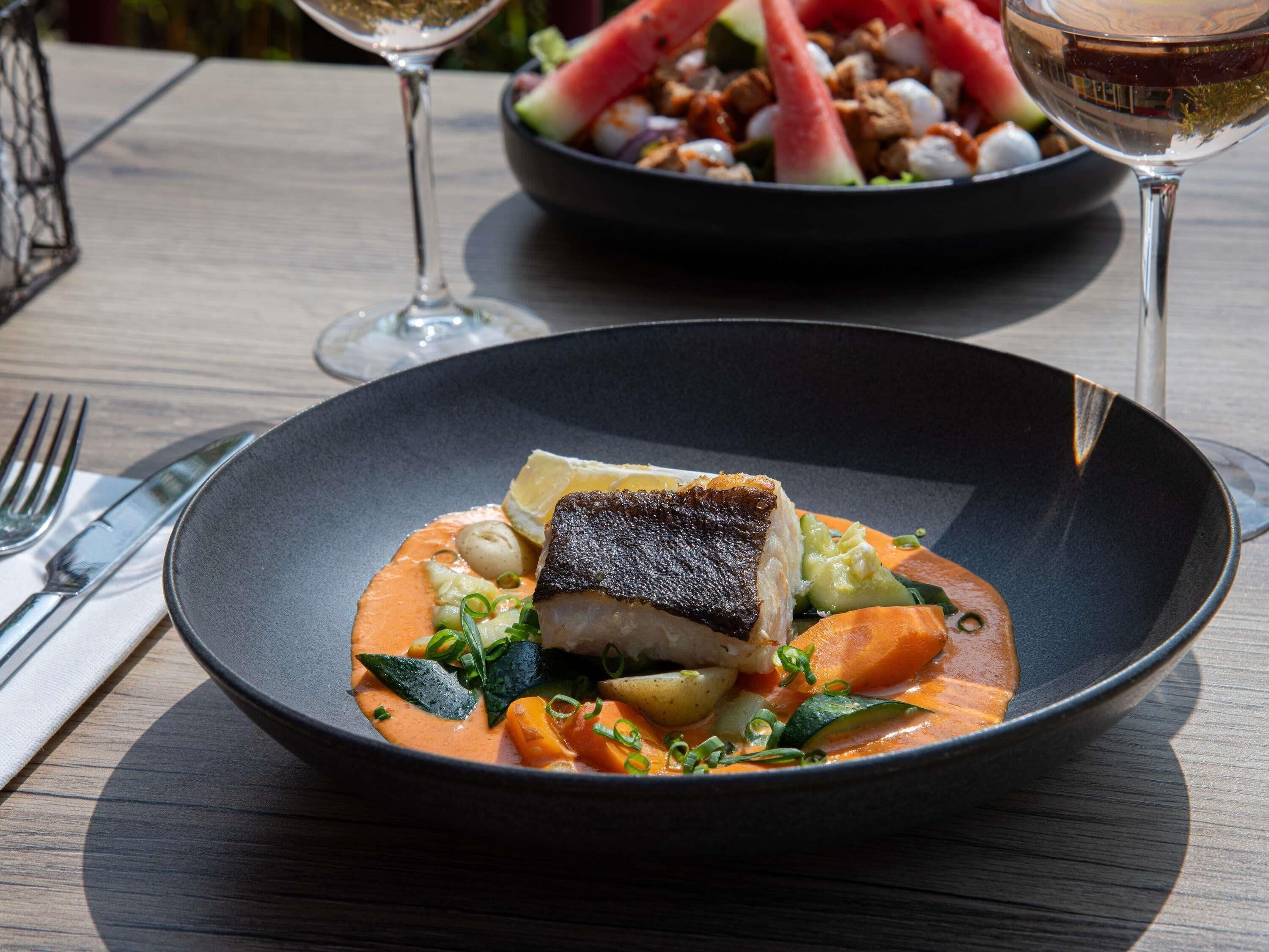 Une table à manger avec une assiette de nourriture, une fourchette, un couteau et deux verres de vin.