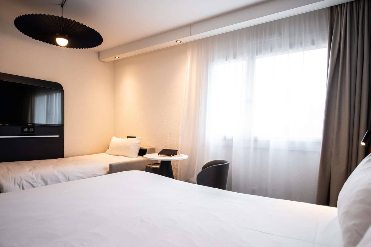 A hotel room with a large bed, a desk with a chair, a television, and a window with curtains.
