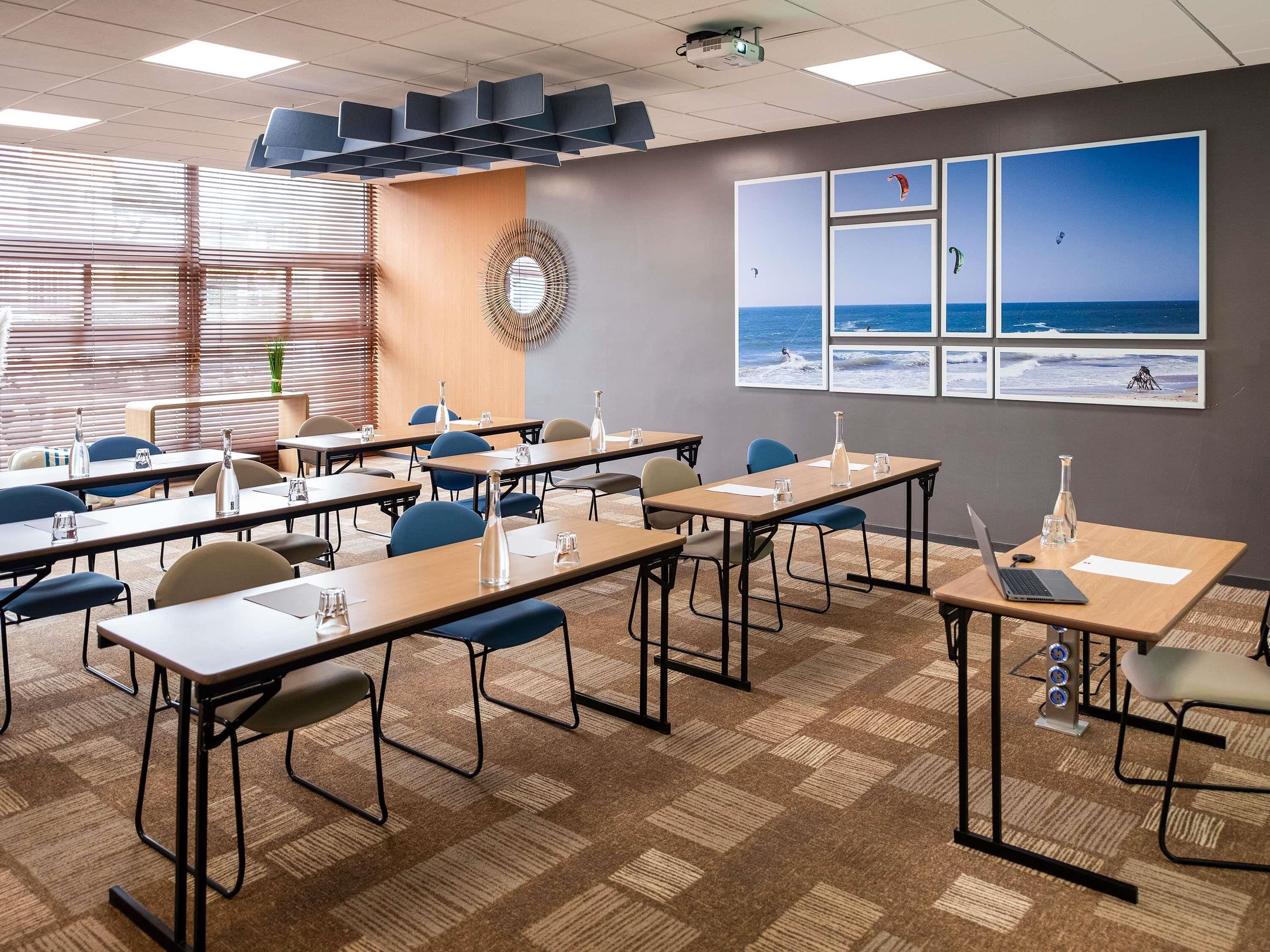 A conference room with tables, chairs, a projector, and a wall with framed pictures of the sea.