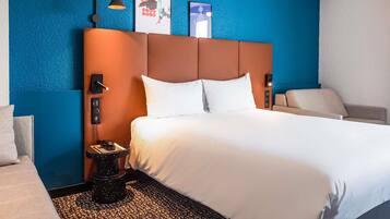 Hotelkamer met een groot bed, een nachtkastje met lamp, een stoel en een muur met kunstwerk.