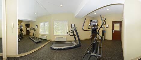A fitness room with a treadmill, elliptical, and mirrored walls.