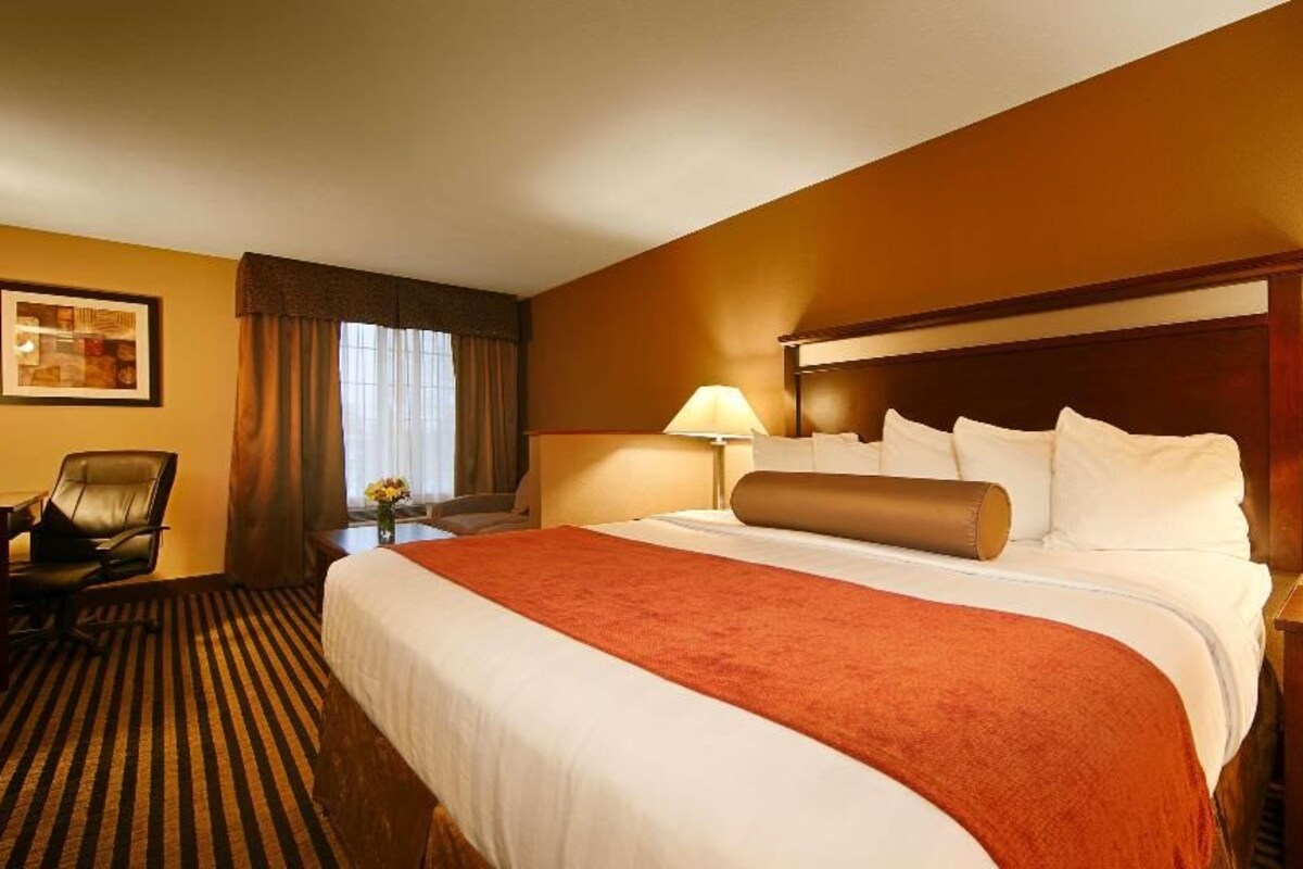A hotel room with a large bed, two bedside tables, a chair, a desk, and a lamp.