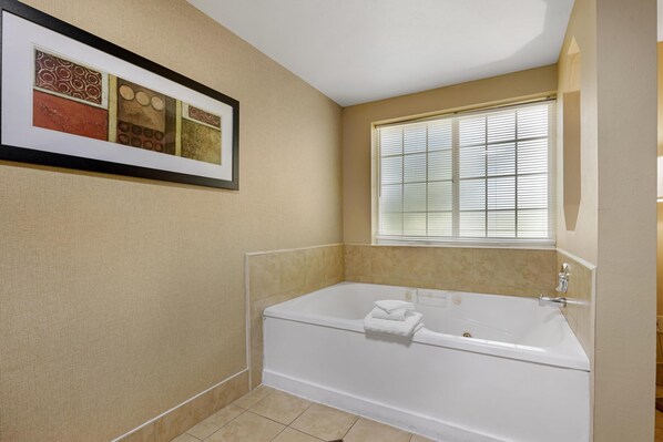 A bathroom with a bathtub, a window with blinds, and a framed picture on the wall.