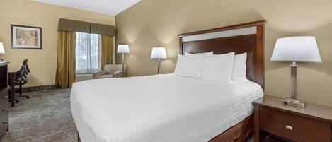 A hotel room with a large bed, two bedside tables with lamps, a desk with a chair, and a window with curtains.