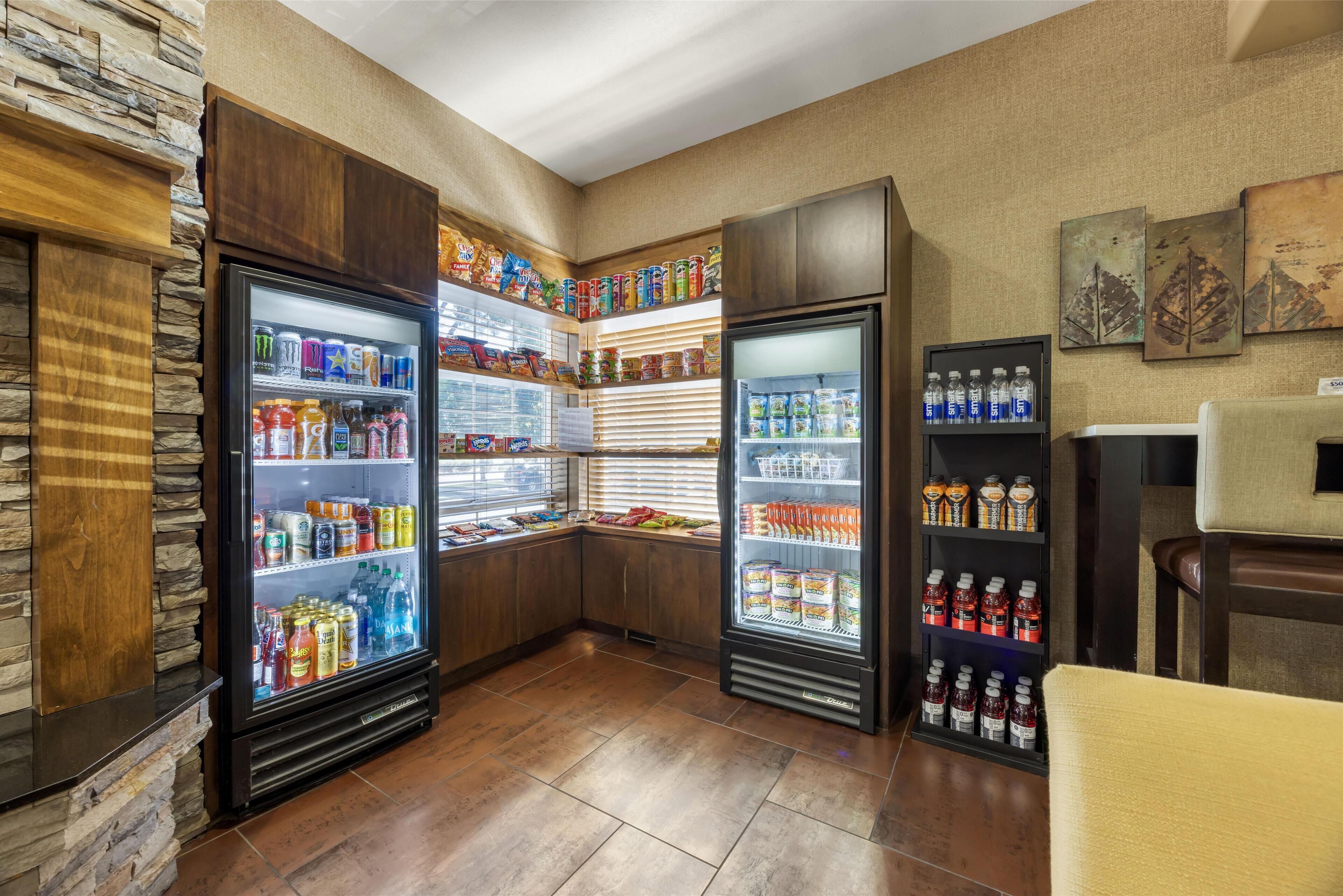 A corner with two beverage dispensers stocked with various drinks, a snack shelf, and a seating area with a chair.