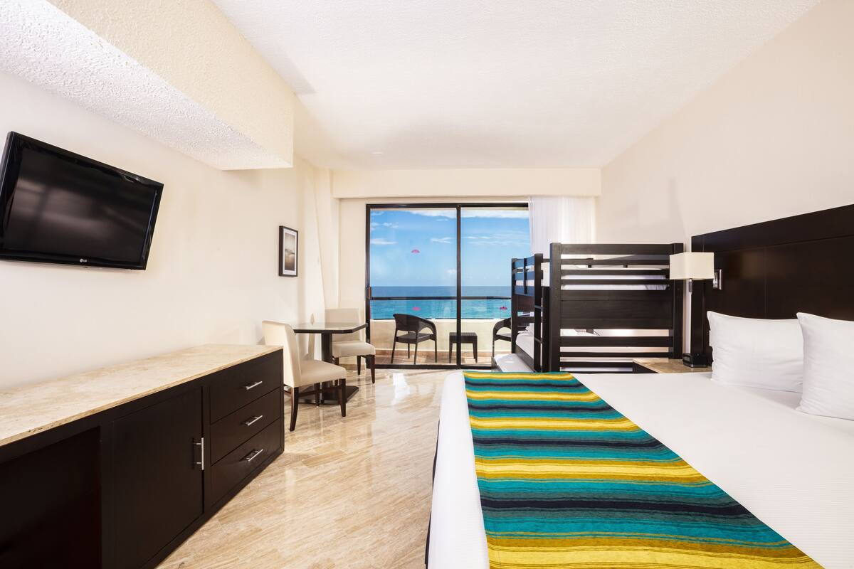 Una camera d'albergo con un letto, una scrivania, una sedia, una televisione e un balcone vista oceano.