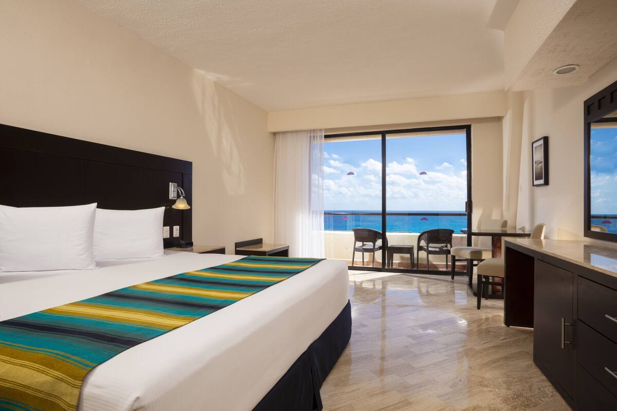 Una camera d'albergo con un letto grande, una scrivania, una sedia e vista sull'oceano.