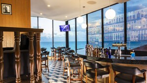 Angolo bar con vista sul mare, sgabelli da bar, televisore e una grande vetrina con bottiglie.