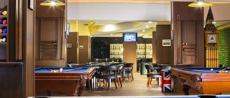 A pool table with balls, a billiard table, and a television screen in a room with wooden walls and ceiling.