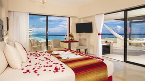 Una camera d'albergo con un letto grande, una TV, un balcone vista oceano e un'area pranzo con tavolo e sedie.