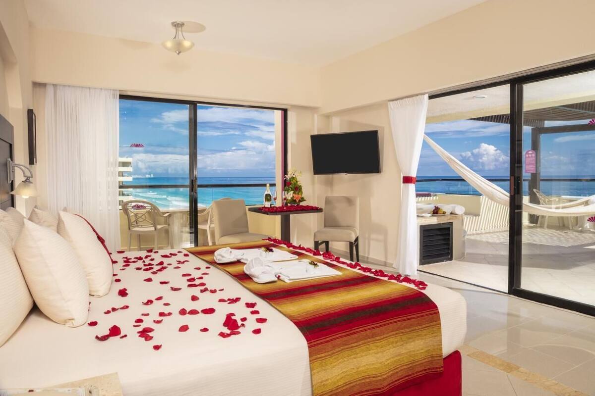 Una camera d'albergo con un letto grande, una TV, un balcone vista oceano e un'area pranzo con tavolo e sedie.