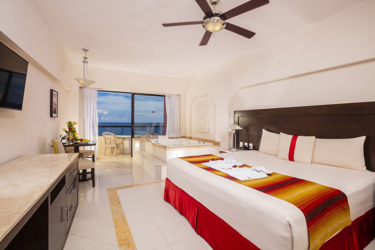 Camera d'albergo con un letto grande, una scrivania, una sedia, una televisione, un ventilatore a soffitto e vista sull'oceano.