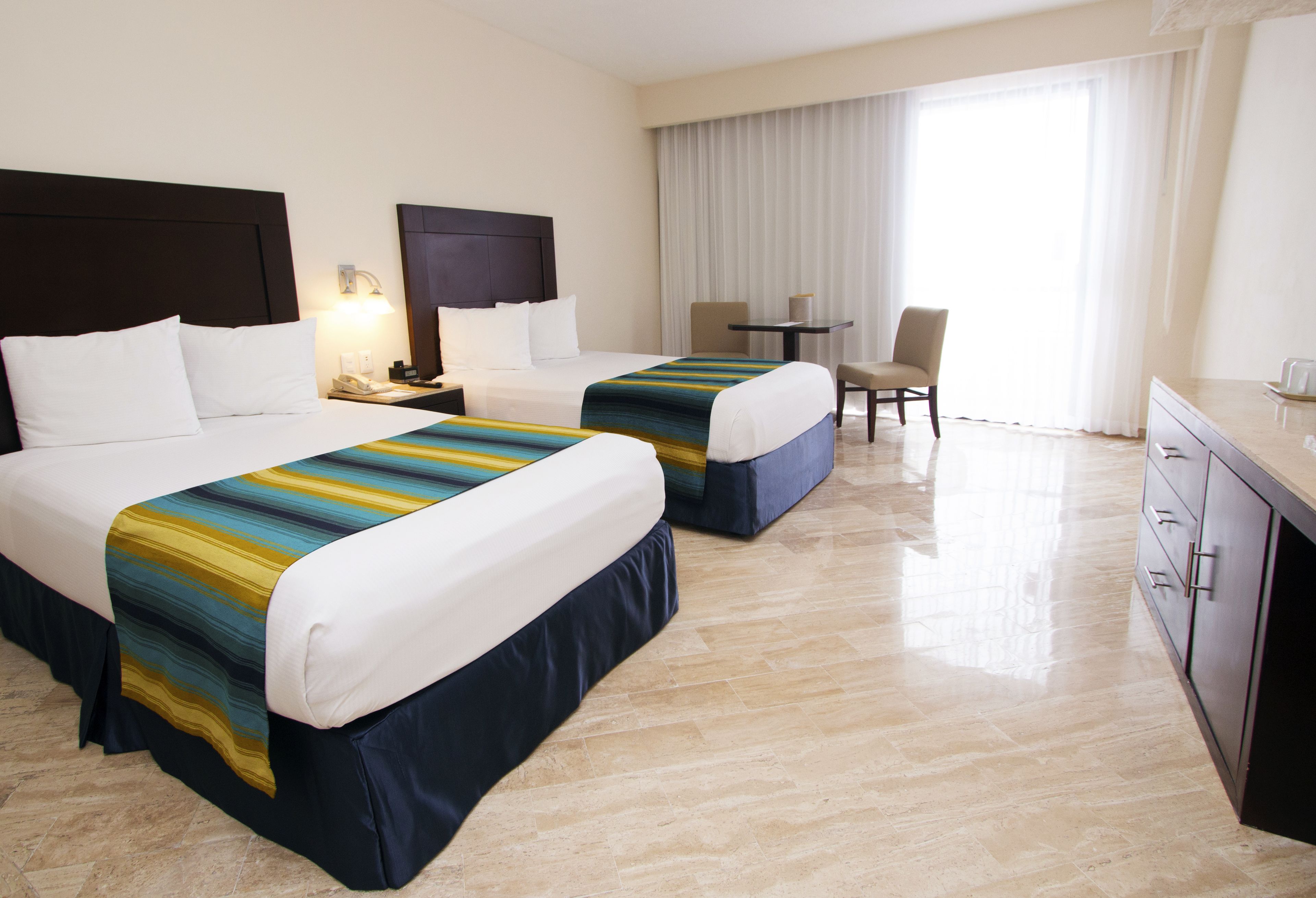 Una camera d'albergo con due letti, una scrivania, una sedia e un minibar.