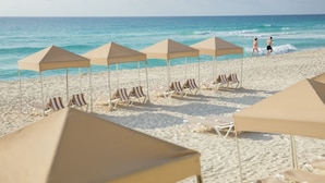 A beach with rows of sun loungers and umbrellas, a clear sky, and the ocean in the background. - Crown Paradise Club Cancun All Inclusive (Cancun)