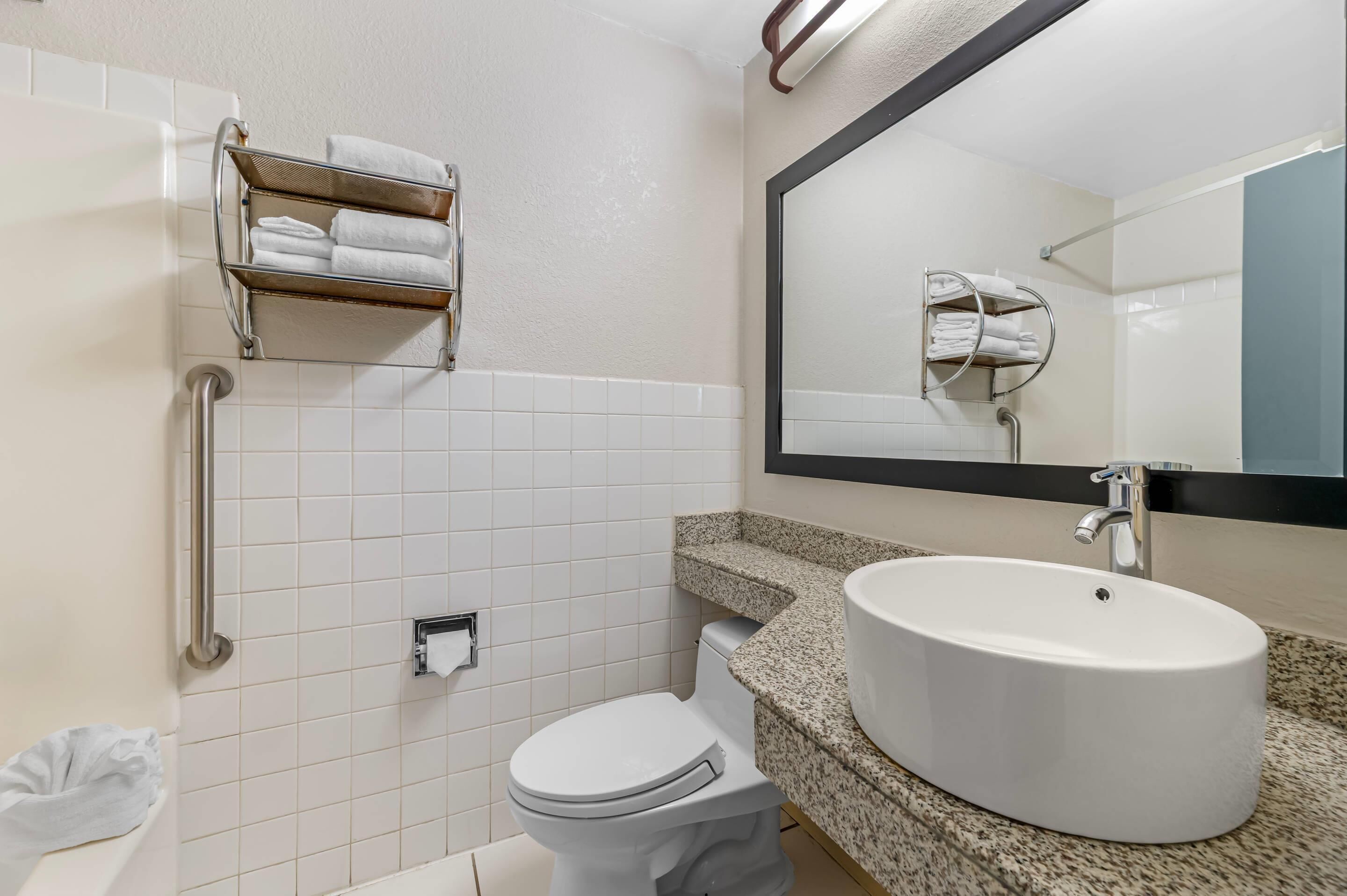 A bathroom with a white toilet, a sink with a large mirror, and a towel rack.