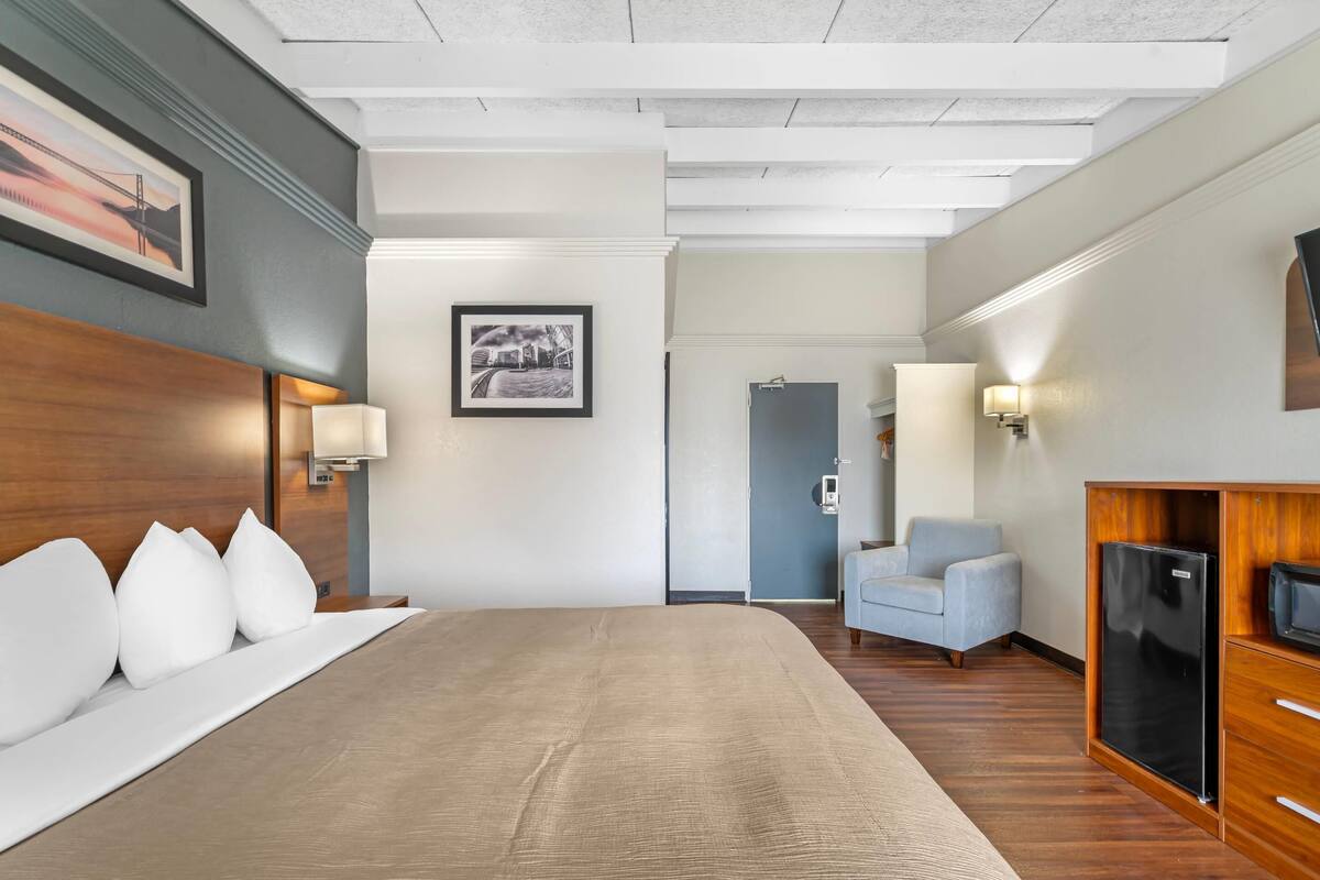 Une chambre d’hôtel avec un grand lit, un bureau avec un ordinateur, une chaise, une télévision et une porte donnant sur une salle de bain.