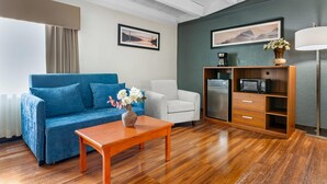 Una sala de estar con sofá azul, sillón blanco, mesa de centro de madera y un mueble con microondas.