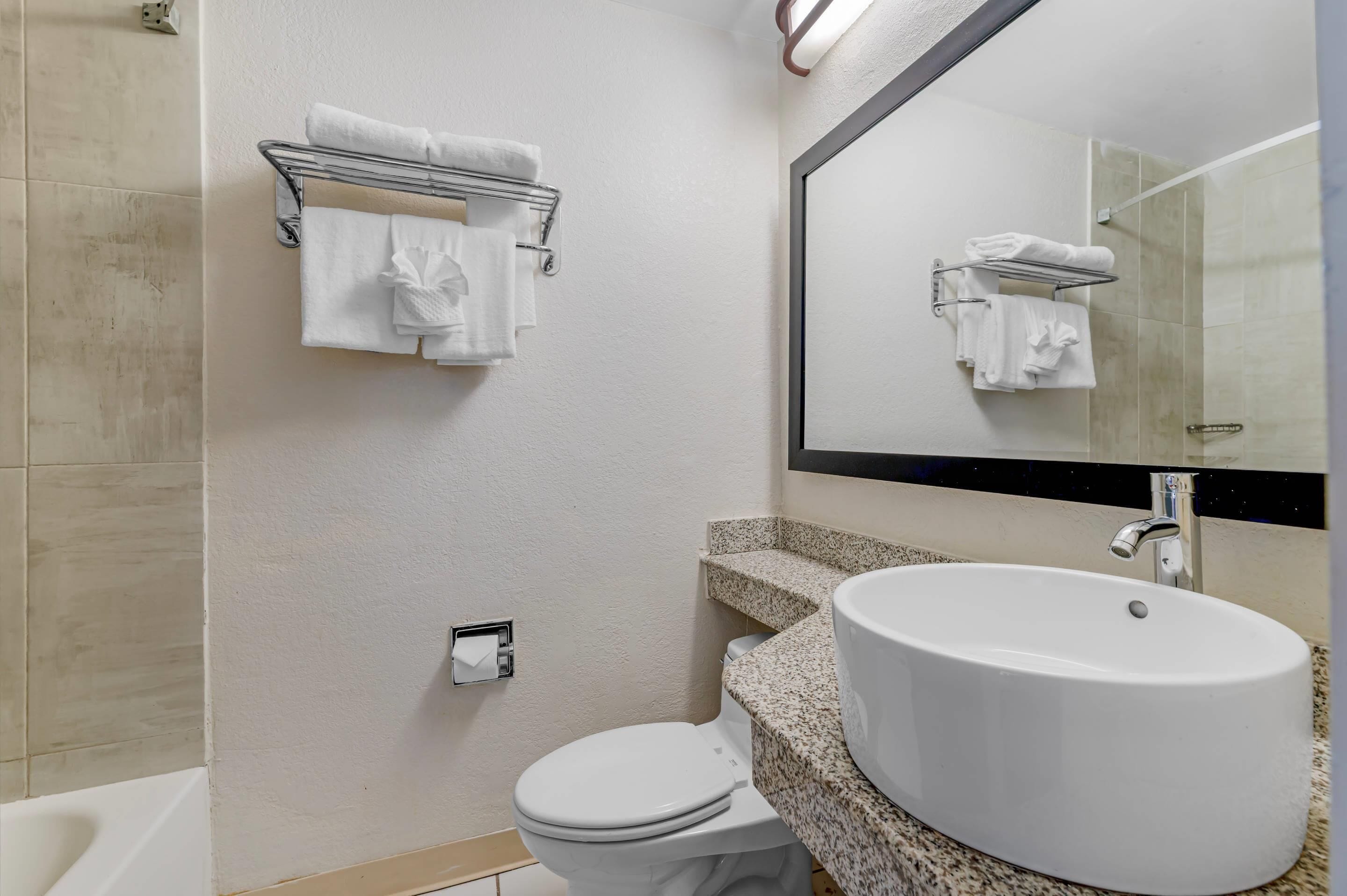 Ein Badezimmer mit einem weißen Waschbecken, einer Toilette, einem Handtuchhalter und einem Spiegel.