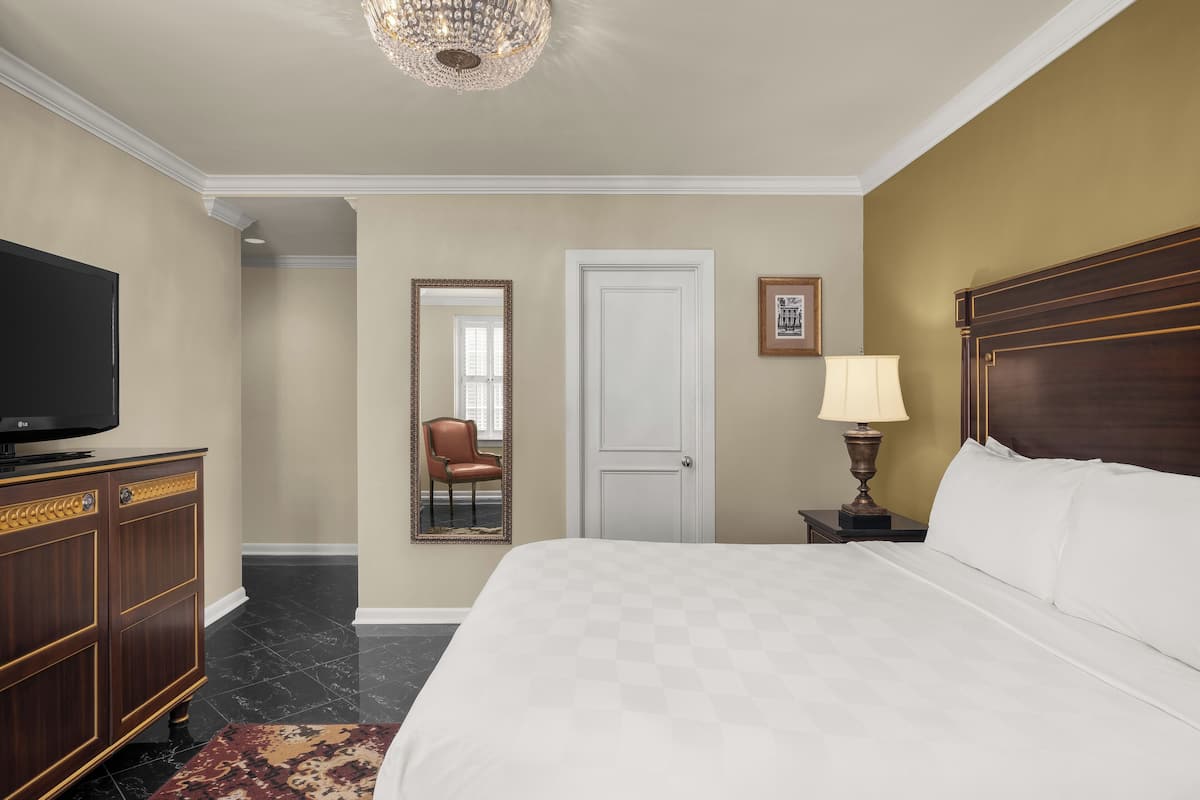 Une chambre d’hôtel avec un grand lit, un téléviseur posé sur une commode en bois, une lampe et un tableau encadré au mur.