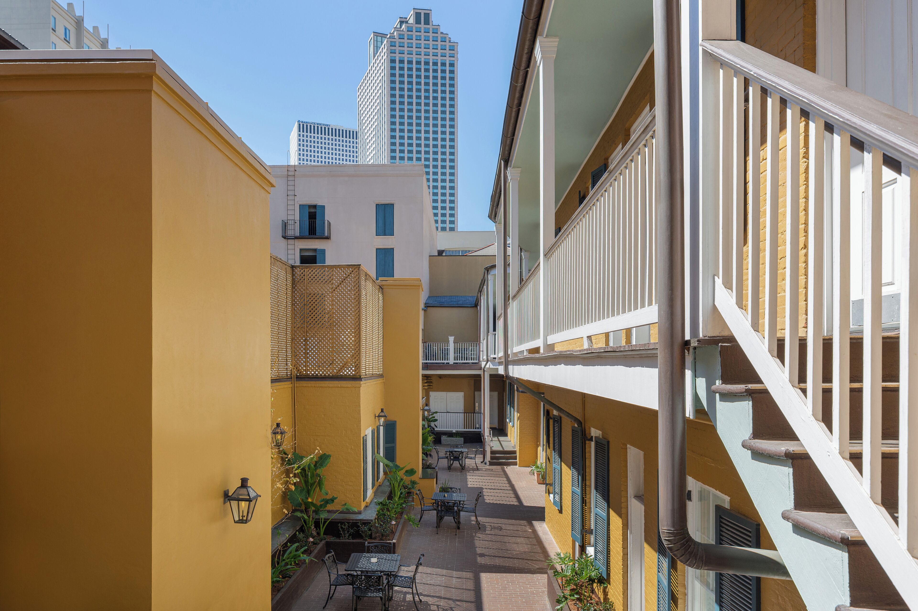 Une cour étroite aux murs jaunes, avec des sièges en plein air et un escalier.