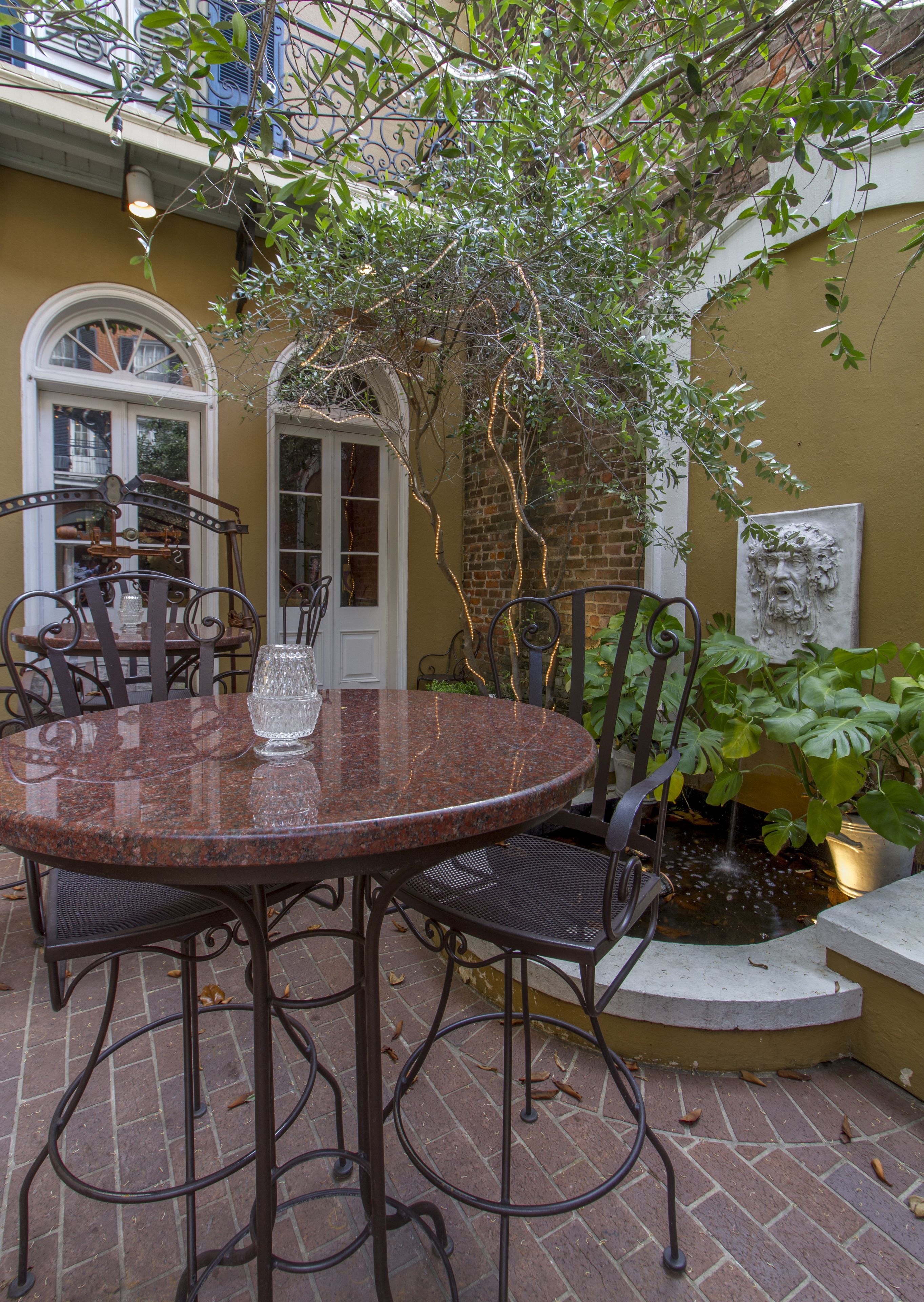 Un patio con una mesa redonda y sillas, una planta en maceta y una pequeña fuente.