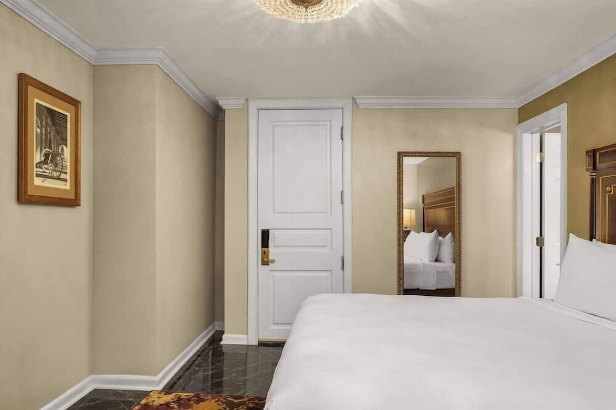 Une chambre d’hôtel avec un lit, une porte, un miroir et un tableau encadré au mur.