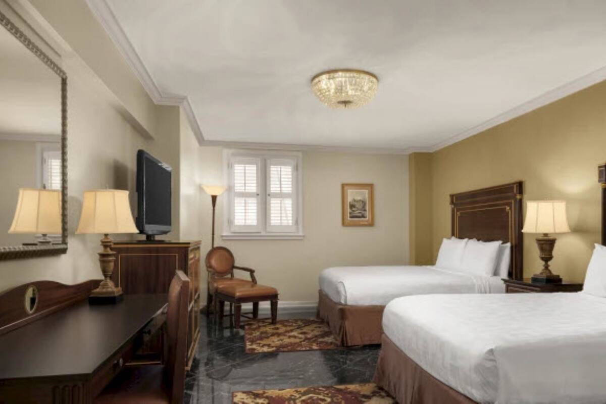 Une chambre d’hôtel avec deux lits, un bureau, une chaise, une télévision et un lustre.