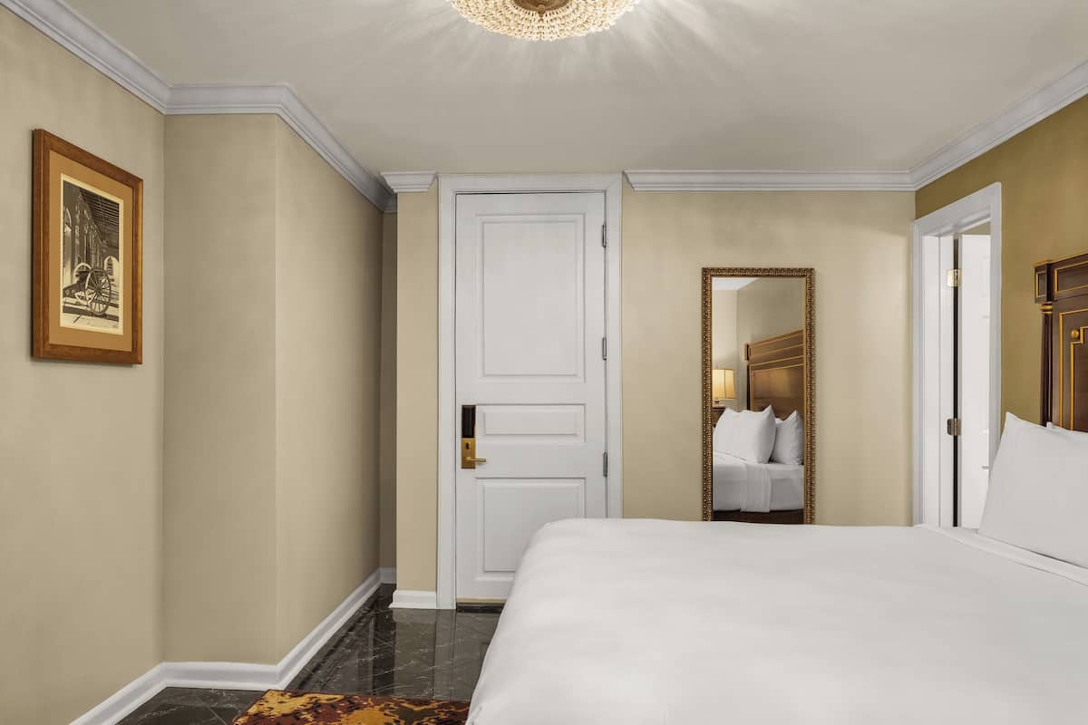 Une chambre d’hôtel avec un grand lit, une porte, un miroir et un tableau encadré au mur.