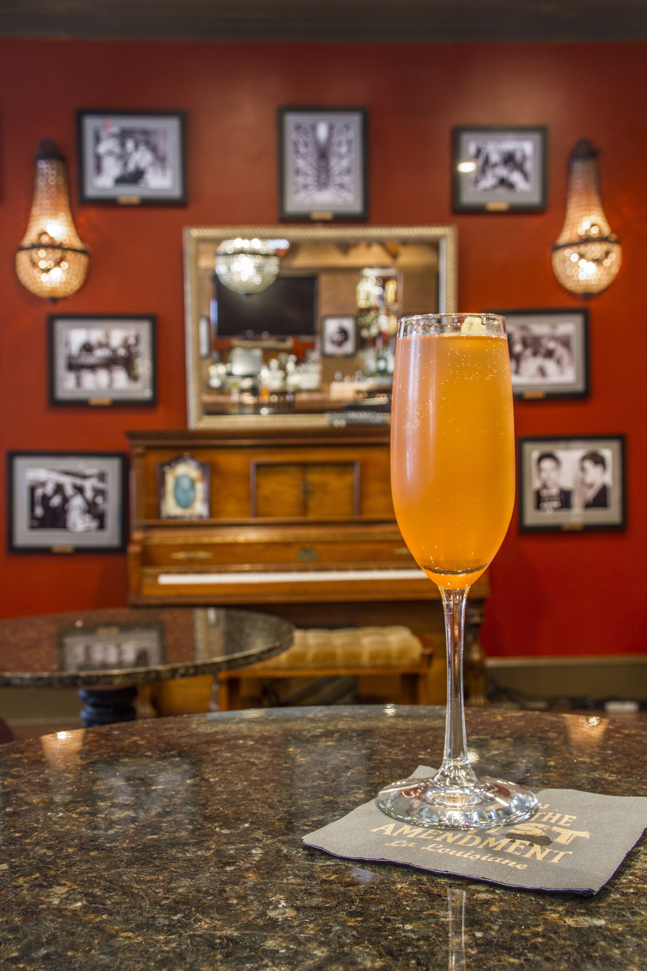Un bar avec un verre contenant une boisson à l’orange, un miroir, des photos encadrées et un meuble en bois.