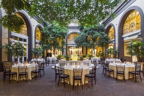 A spacious courtyard with round tables set for dining, surrounded by arches and potted plants. - Hotel Mazarin (New Orleans)