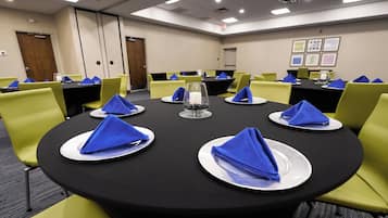 Un salón de conferencias con mesas redondas, cada una con platos blancos, servilletas azules y sillas verdes.