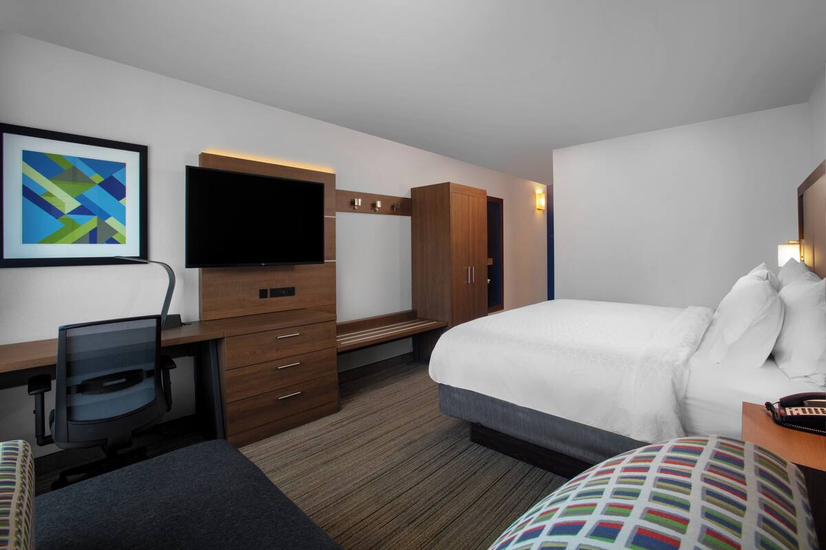 A hotel room with a bed, a desk with a chair, a television, and a wardrobe.