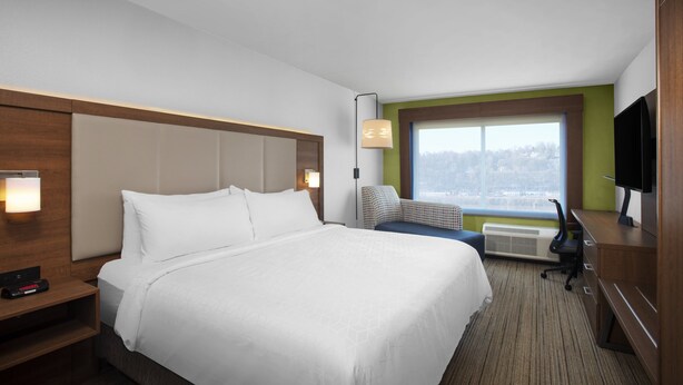 A hotel room with a bed, a desk, a chair, a TV, and a window with a view.