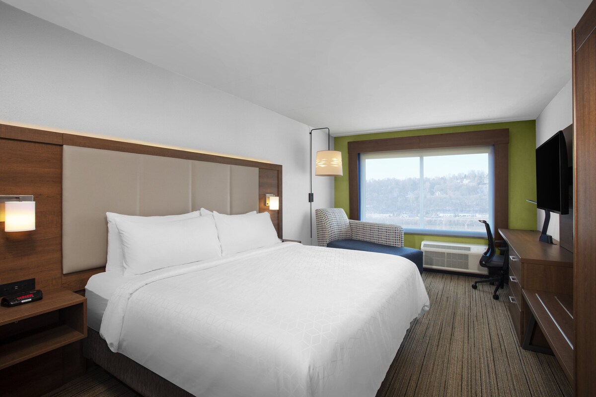 A hotel room with a bed, a desk, a chair, a TV, and a window with a view.