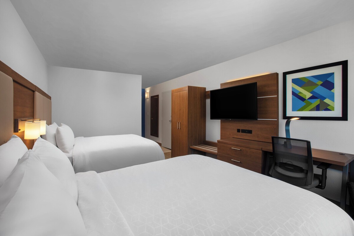 Une chambre d’hôtel avec deux lits, un bureau, une chaise, une télévision et une œuvre d’art encadrée au mur.