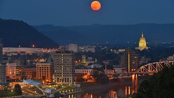 A cityscape at dusk with a prominent moon in the sky, a bridge, and a river reflecting city lights.