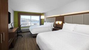 A hotel room with two beds, a desk, a chair, a TV, a window with a city view, and a lamp.