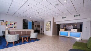A modern lobby with a reception desk, seating area, and a colorful wall decoration.
