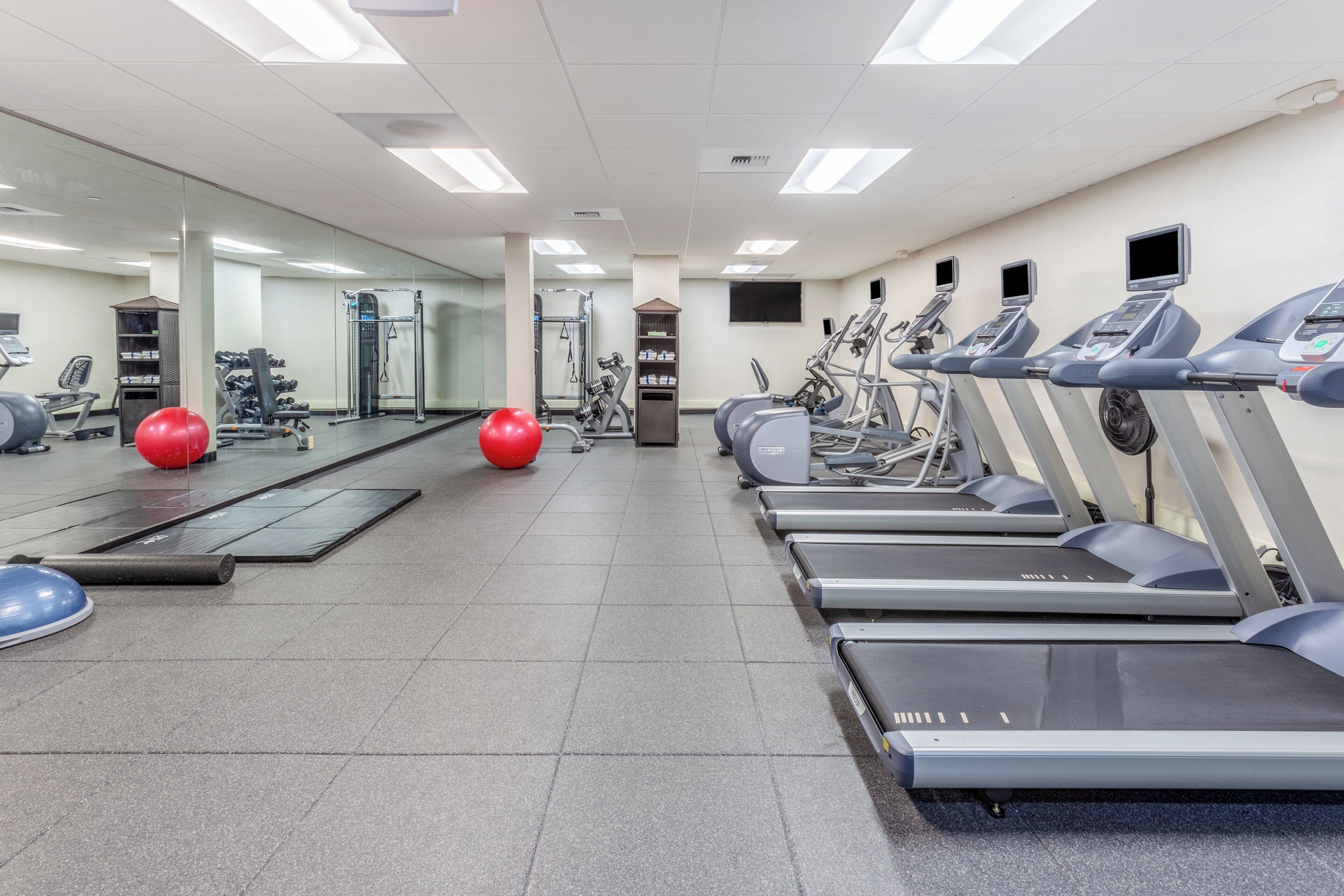 Een fitnessruimte met loopbanden, gewichten en fitnessballen.