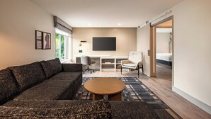 A modern living room with a sectional sofa, a round coffee table, a white armchair, and a TV mounted on the wall. - Holiday Inn Downtown - Missoula by IHG (Missoula)