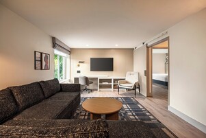 A modern living room with a sectional sofa, a round coffee table, a white armchair, and a TV mounted on the wall.